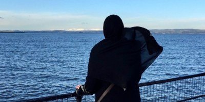 a muslim woman in hijab looking at the blue water and sky
