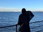 a muslim woman in hijab looking at the blue water and sky