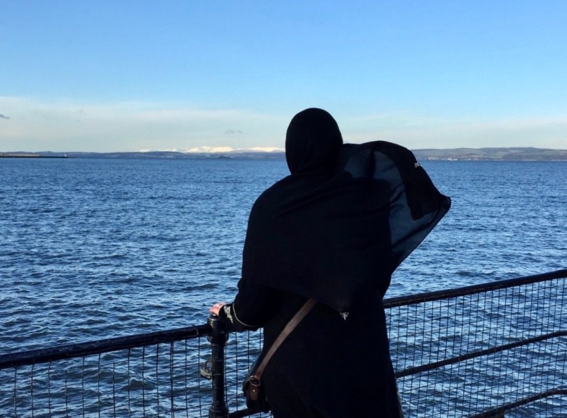 a muslim woman in hijab looking at the blue water and sky